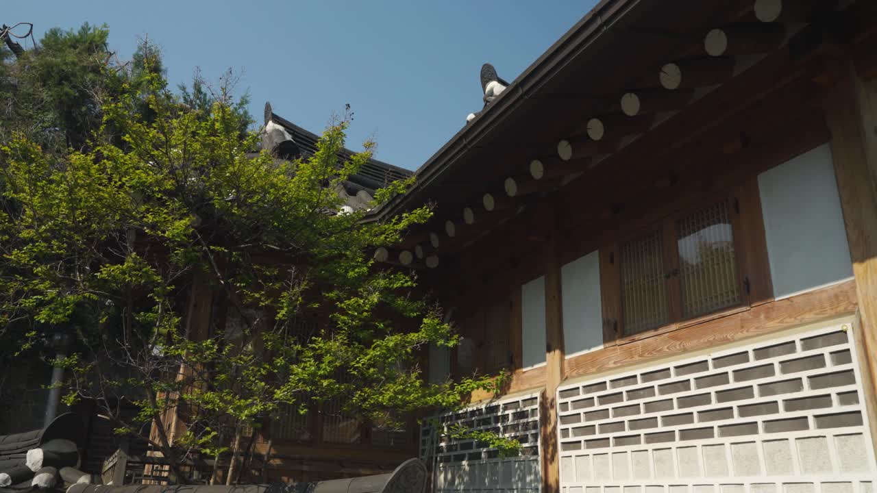 A dynamic parallax shot captures the unique details of a traditional Korean Hanok roofline, emphasizing its curved tiles, wooden beams, textured walls in Bukchon Hanok Village, Seoul, South Korea