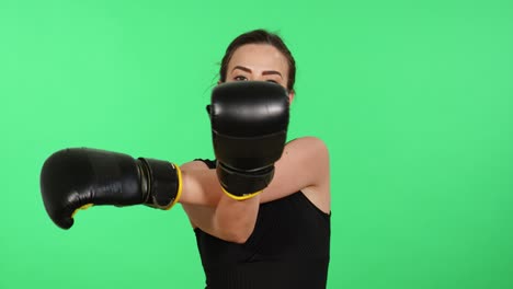 Atractiva-Mujer-Morena-Con-Guantes-De-Boxeo-Mira-Hacia-La-Cámara-Mientras-Estira-Los-Brazos-Con-Pantalla-Verde-En-El-Fondo