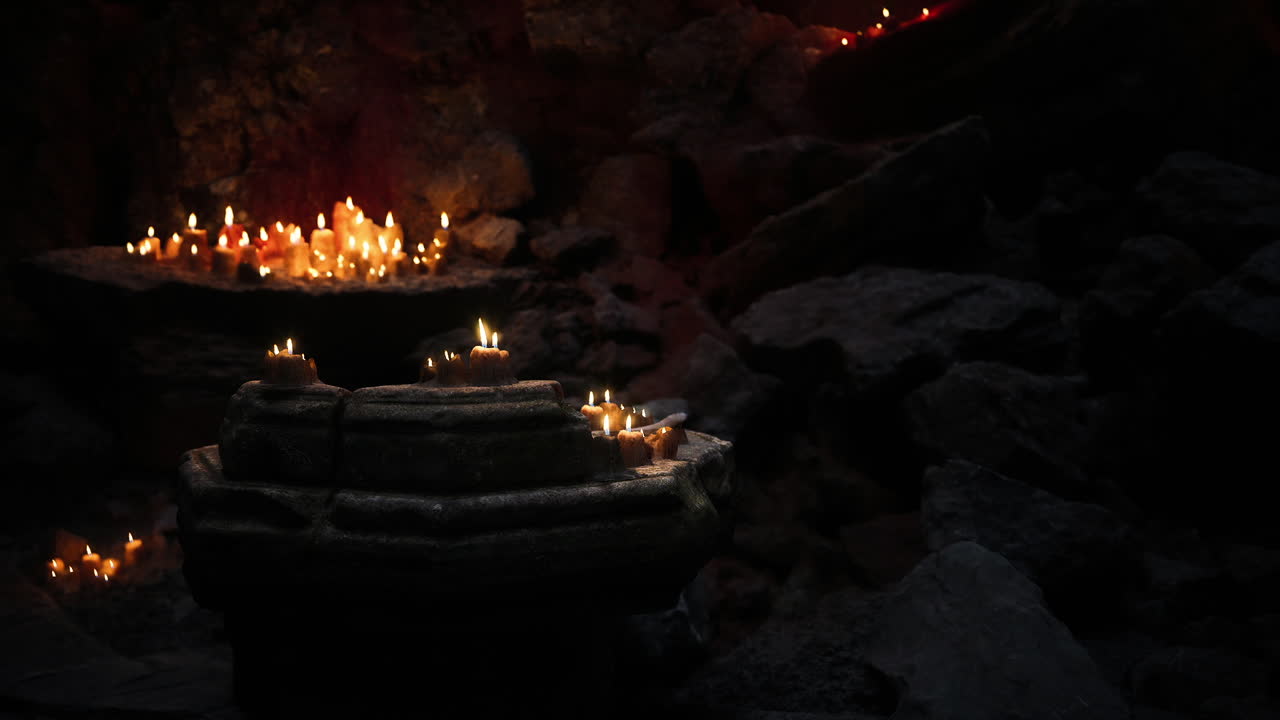 Candles illuminate rock formations in a serene dark cave setting