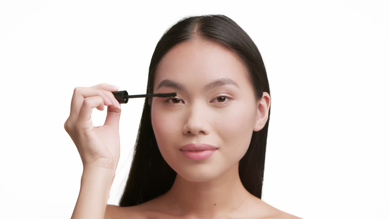 Young Asian woman applying mascara on her eyelashes