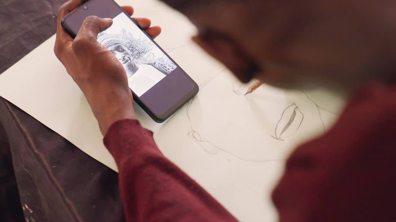 Kunstner skitserer portræt med telefon, blyant og papir. Nærbillede over skulderen af hænder, der tegner bløde konturer, mens smartphonen viser en sort malerireference, varmt studiolys, grafitlinjer.