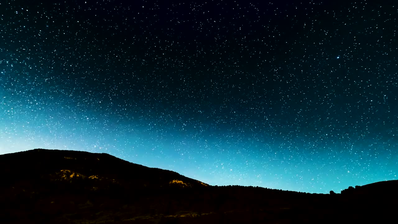 Starry twilight turns dark as the Milky Way core rises above the silhouetted landscape - time lapse