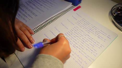 closeup de las manos de la chica con anillos mientras continúa escribiendo notas en papel gráfico con pluma azul tarde en la noche