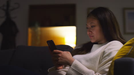 woman spending evening at home on sofa putting in wireless earbuds and streaming music or podcast from mobile phone 4