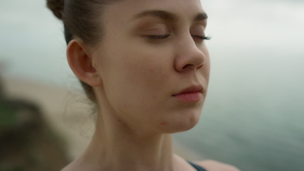 una chica de ojos cerrados meditando en la playa de cerca. una mujer respirando practicando yoga.