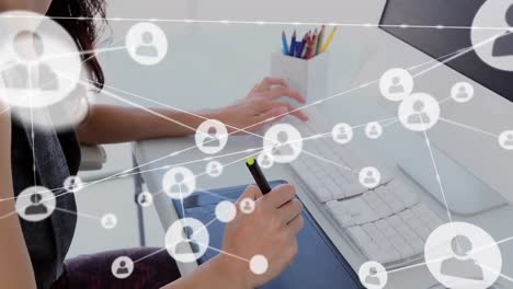 animation of network of profile icons over mid section of a woman using graphic tablet at office