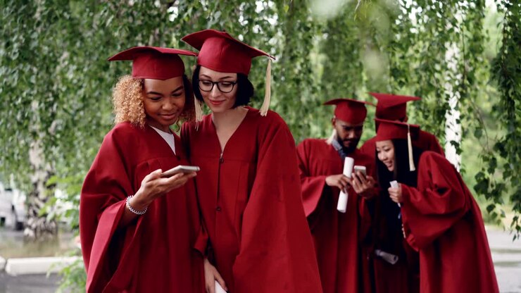 Belle giovani studentesse laureate si scattano un selfie con lo smartphone e poi guardano le fotografie. Concetto di tecnologia moderna, millennial e istruzione.
