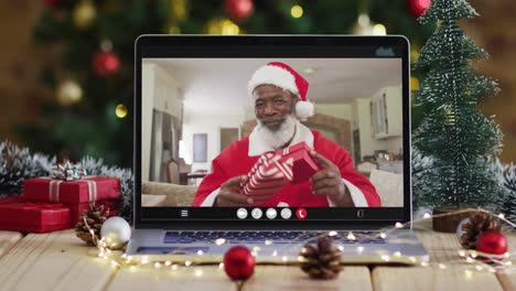 Älterer-Afroamerikanischer-Mann-Im-Weihnachtsmannkostüm-Bei-Videoanruf-Auf-Laptop,-Mit-Weihnachtsbaum