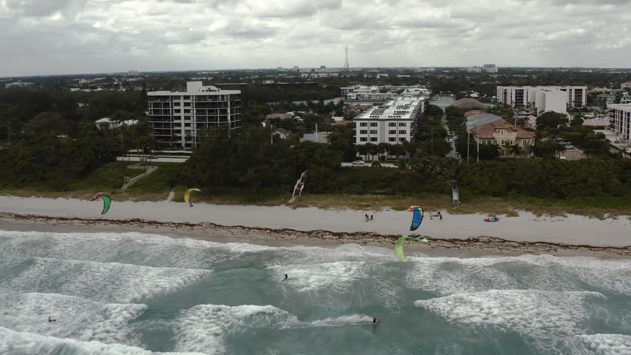 Vídeo aéreo ascendiendo sobre múltiples practicantes de kitesurf mientras navegan entre sí.