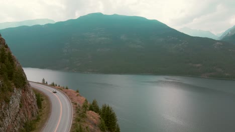 Toma-Aérea-De-Seguimiento-De-Un-Automóvil-Que-Pasa-Por-El-Lago-Slocan