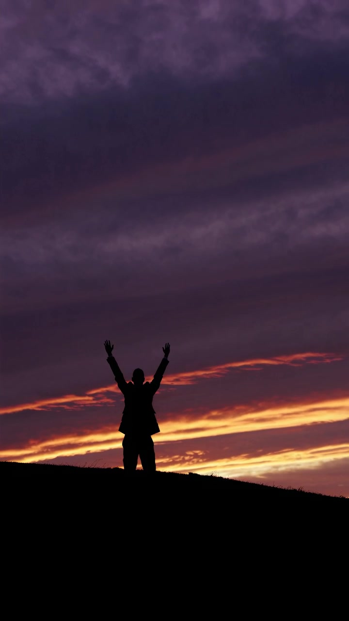 Silhouette di una persona in piedi con le braccia alzate contro un cielo al tramonto