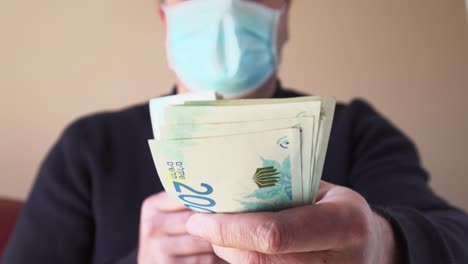 현금 셰 - 이스라엘 통화, 종이 지폐를 주는 모습 - 유행병 기간 동안 보호 얼굴 마스크를 입은 이스라엘 남자가 청구서를 지불하는 클로즈업