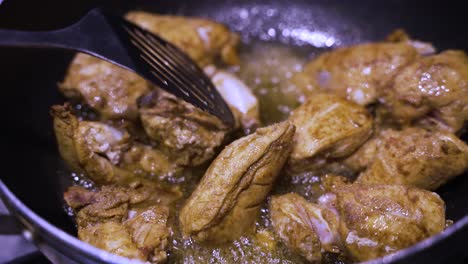 spicy chicken pieces sizzling in oil and being stirred by metal slotted spatula