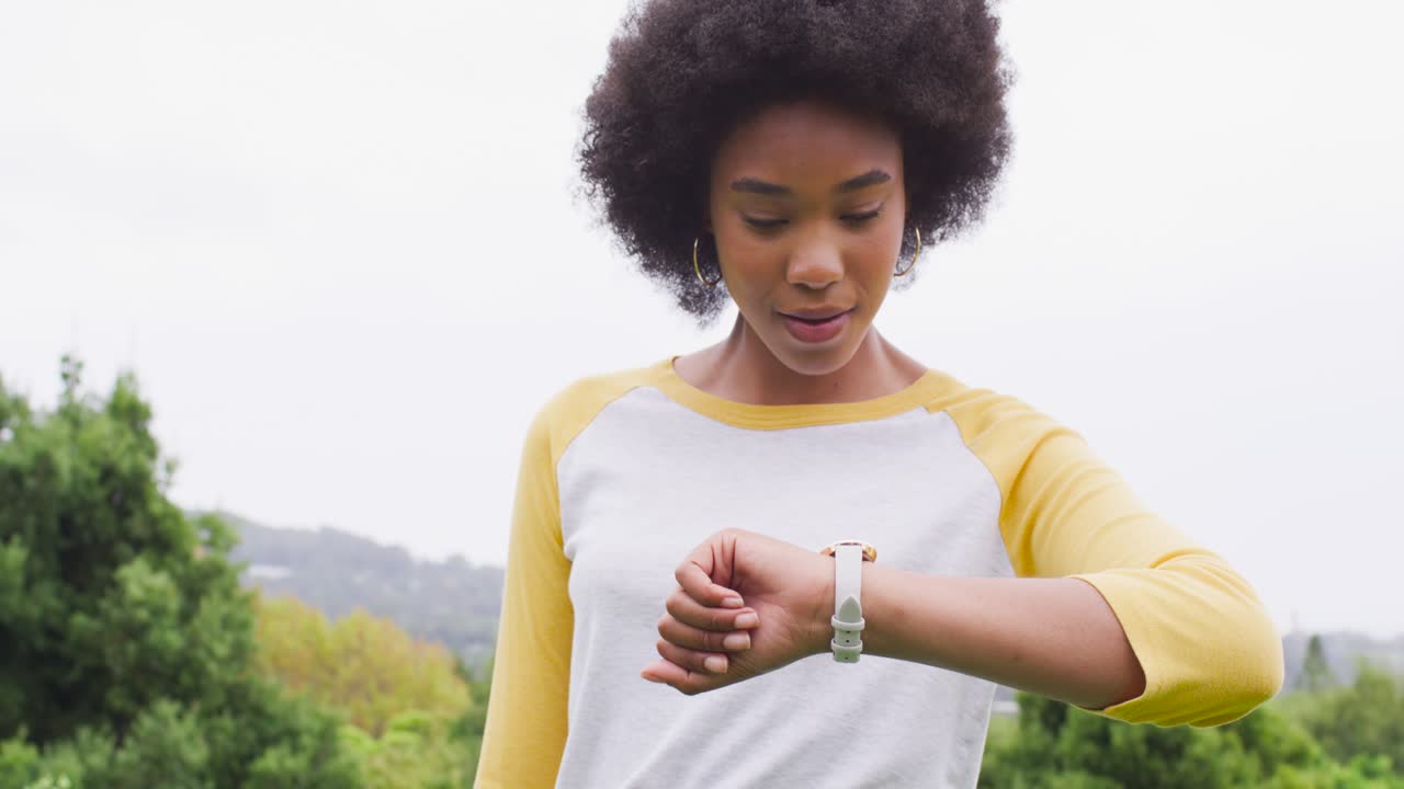 African American woman lifting to watch with yellow-sleeves, checking as camera moving up in park