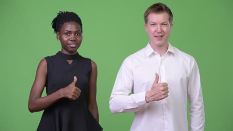 two young multi-ethnic business couple giving thumbs up together