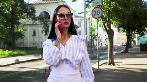 stylish brunette in sunglasses standing at urban street and talk on phone