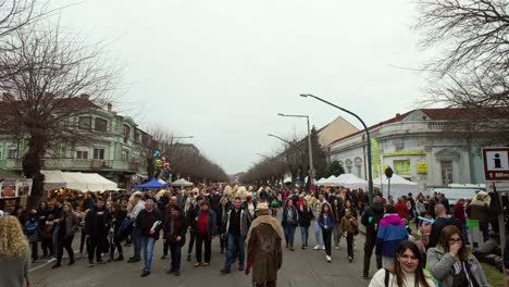 main street of mohacs during the busó-walking festival, where the locals in scary sheepskin costumes and masks walk in the crowd among the visitors in hungary.