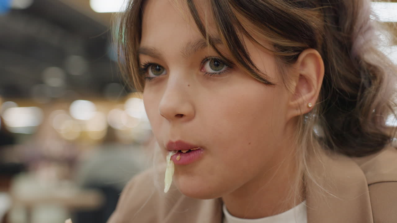 젊은 사람이 패스트푸드를 즐기고 있어요. 젊은 친구가 활기 넘치는 쇼핑몰 분위기 속에서 큼지막한 버거를 맛있게 먹고 있네요. 10대 청소년이 북적거리는 푸드 코트에서 소스가 보이는 육즙 가득한 버거를 힘차게 먹고 있어요.