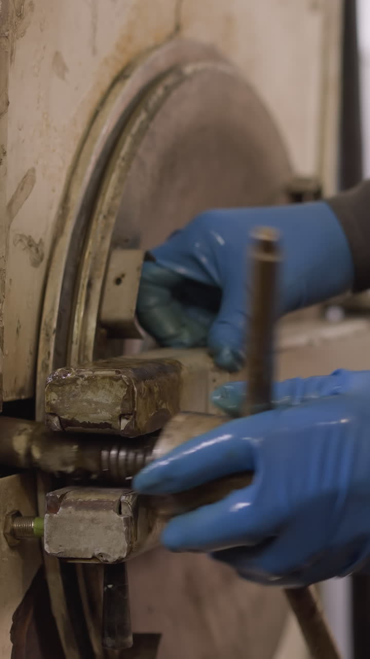 보호 장비를 착용한 노동자, 세라 작업실에서 오븐 치를 수동으로 작동하는 노동자, 레버를 가진 손에 초점을 맞추십시오.