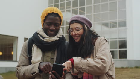 cheerful diverse couple using smartphone and discussing route in city