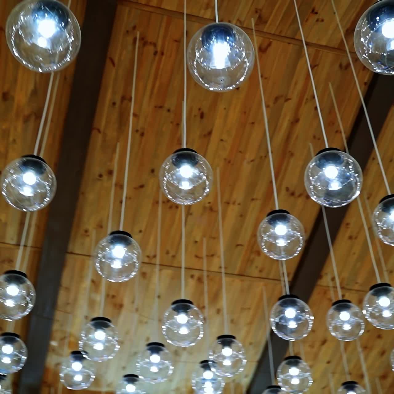 Lamps hanging on celling. Wood background. Warm light. Modern design. Transparent round glass celling lamps. Wooden celling. Modern design. Video from below.