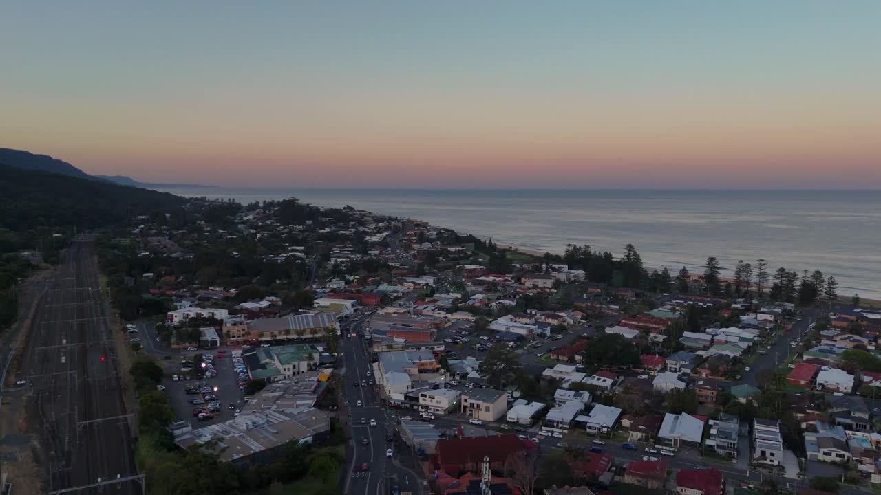 vista aérea de thirroul al amanecer, mostrando la ciudad costera bañada en la suave luz de la mañana y el vasto océano más allá