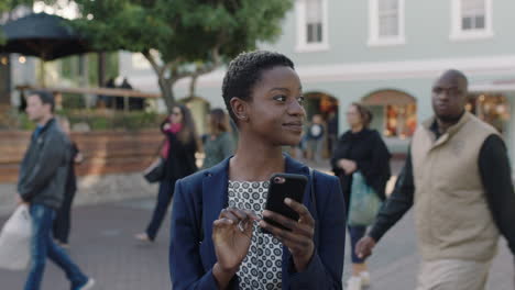 Retrato-De-Cerca-De-Una-Mujer-De-Negocios-Afroamericana-Sonriendo-Feliz-Usando-Mensajes-De-Texto-En-Un-Teléfono-Inteligente-Navegando-En-La-Ciudad