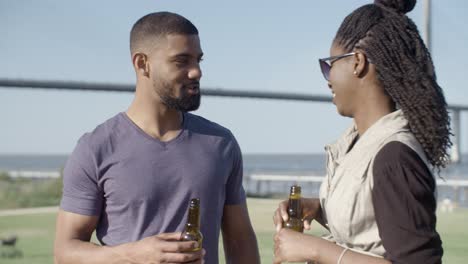 una feliz pareja afroamericana hablando mientras beben cerveza.