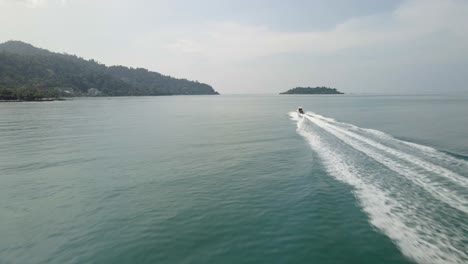 aerial drone follow shot of a speed boat traveling fast towards an island in a tropical sea with mountain coastline