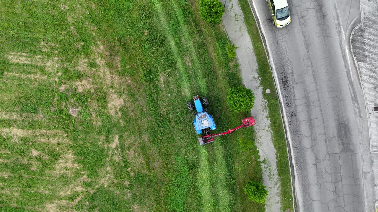 Aerial view of blue agricultural machinery mowing lawn beside suburban roundabout in Piacenza, northern Italian cityscape