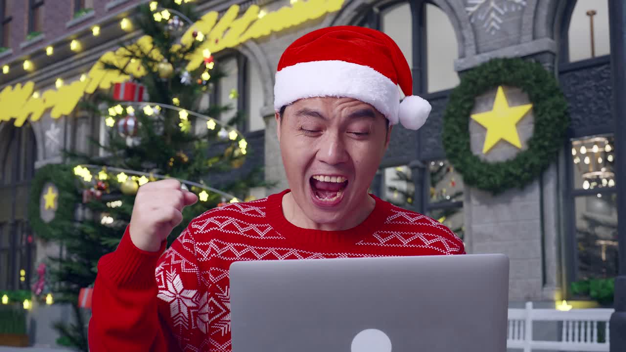 크리스마스 의상을 입은 아시아인 남자가 크리스마스 밤에 서 있는 동안 노트북을 사용하여 성공을 축하하는 미소로 클로즈업