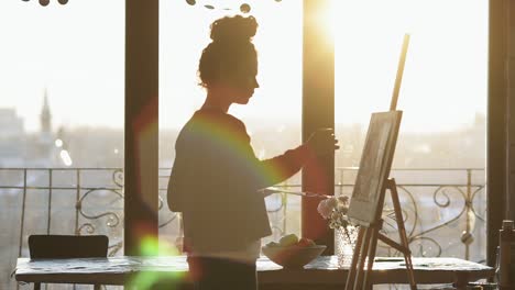 Unrecognizable-figure-of-female-artist-drawing-on-easel-in-an-art-studio-with-panoramic-windows.-Slow-motion.