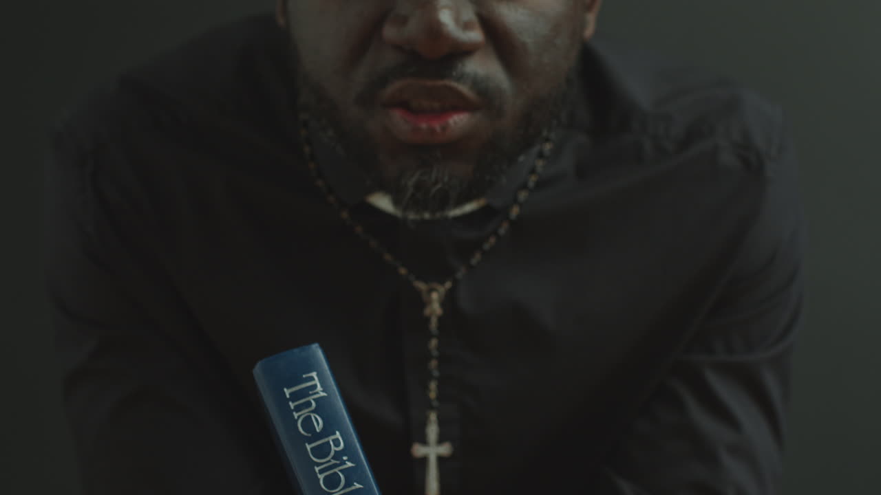 Black Clergyman Holding Bible and Praying to God in Church