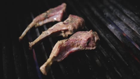 lamb chops roasting on bbq grill in professional kitchen flames kicking up smoking cooking the raw meat on black cast iron grill tight trucking right steady slow motion