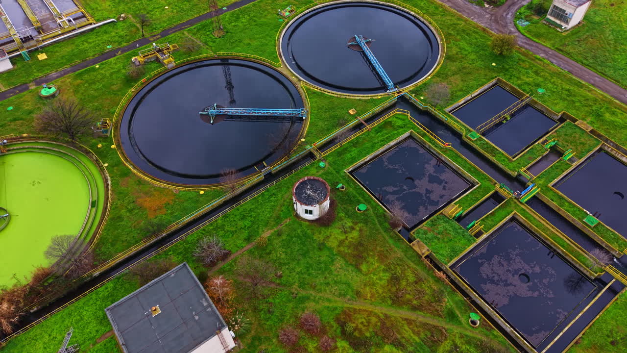 Water treatment facility located in the countryside with circular tanks, green grass, and various structures showing maintenance activities during daylight