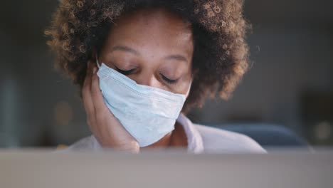 young african businesswoman in protective mask looking at laptop display working with data in office