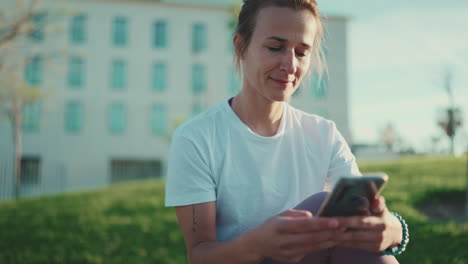 una joven deportiva usando el teléfono en el parque de la ciudad.