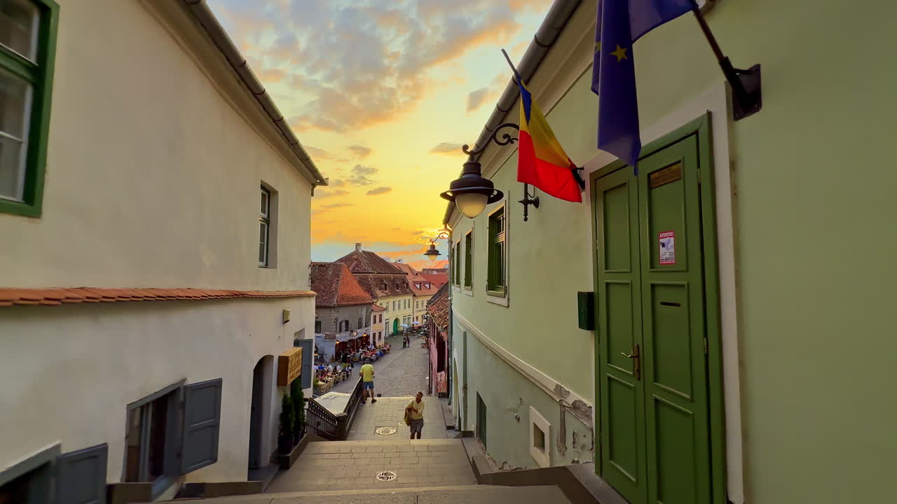 Sibiu, Romania, 1 July 2025: Narrow street with sunset view in Sibiu. Charming narrow street with Romanian and EU flags in Sibiu Romania at sunset