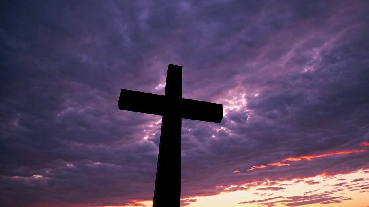 Sagoma di croce cristiana contro un cielo drammatico al tramonto viola e arancione