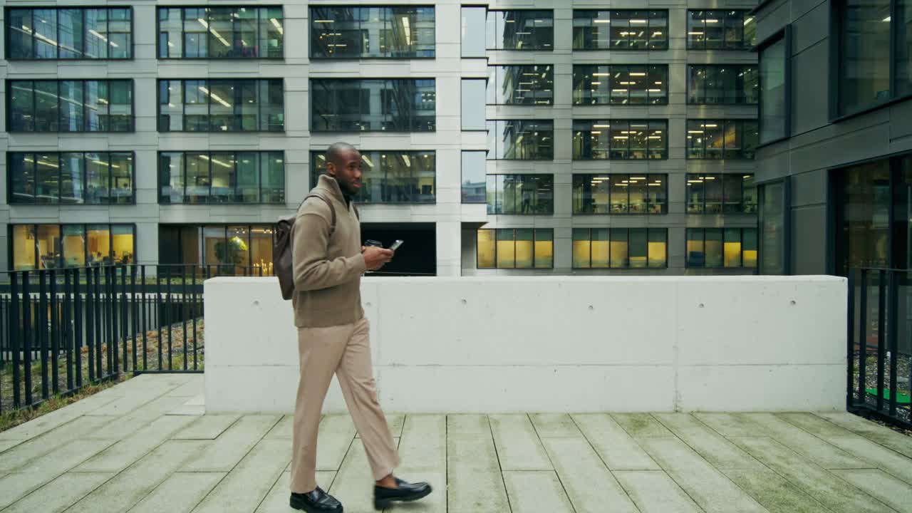uomo che cammina su un patio della città, usando il suo telefono