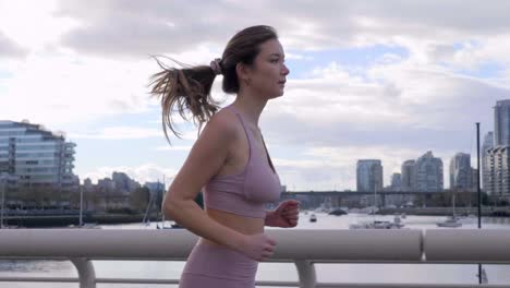 asian woman jogs across bridge in downtown vancouver bc landscape, slowmo