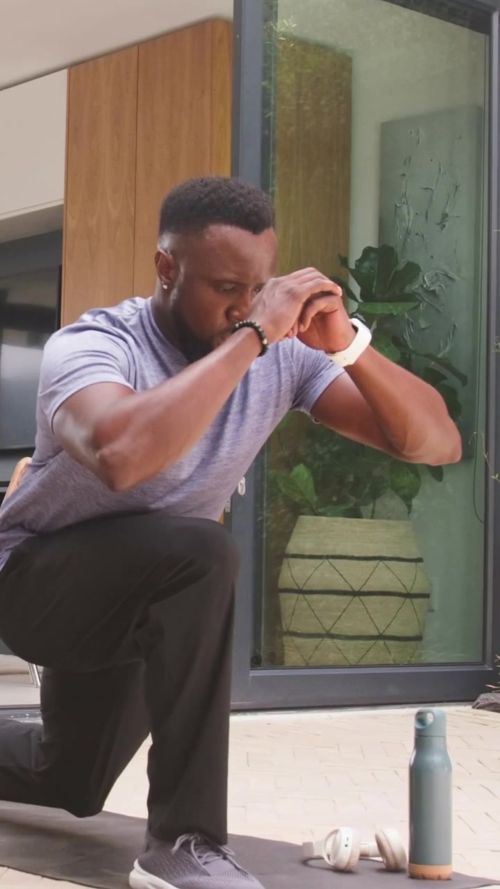 Vertical video: Stepping onto mat, man lunging on patio for workout with weights, wearing gray tee