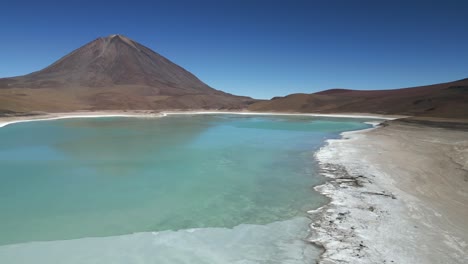 Aerial-drone-pan-shot-from-right-to-left-over-a-large-partly-frozen-lake-at-the-foothill-of-a-mountain-in-Bolivia-on-a-cold-winter-day