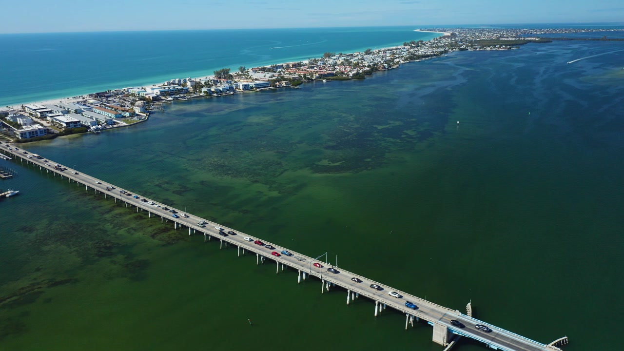 Vehicles travel across a long bridge leading to Bradenton Beach. The scene captures the coastal town and surrounding water, ideal for travel and infrastructure themes.