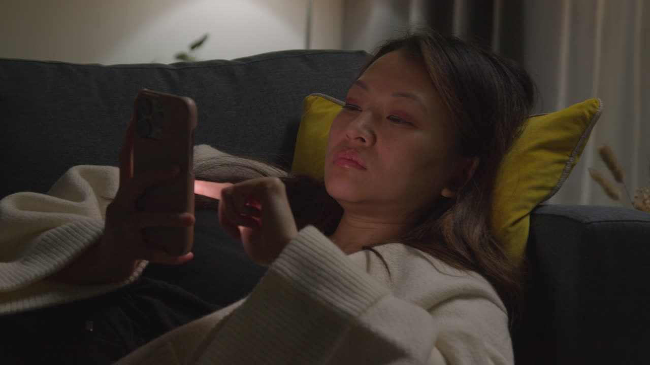 близкий взгляд на женщину, проводящую вечер дома, лежащую на диване с мобильным телефоном, просматривающую интернет или социальные сети 1