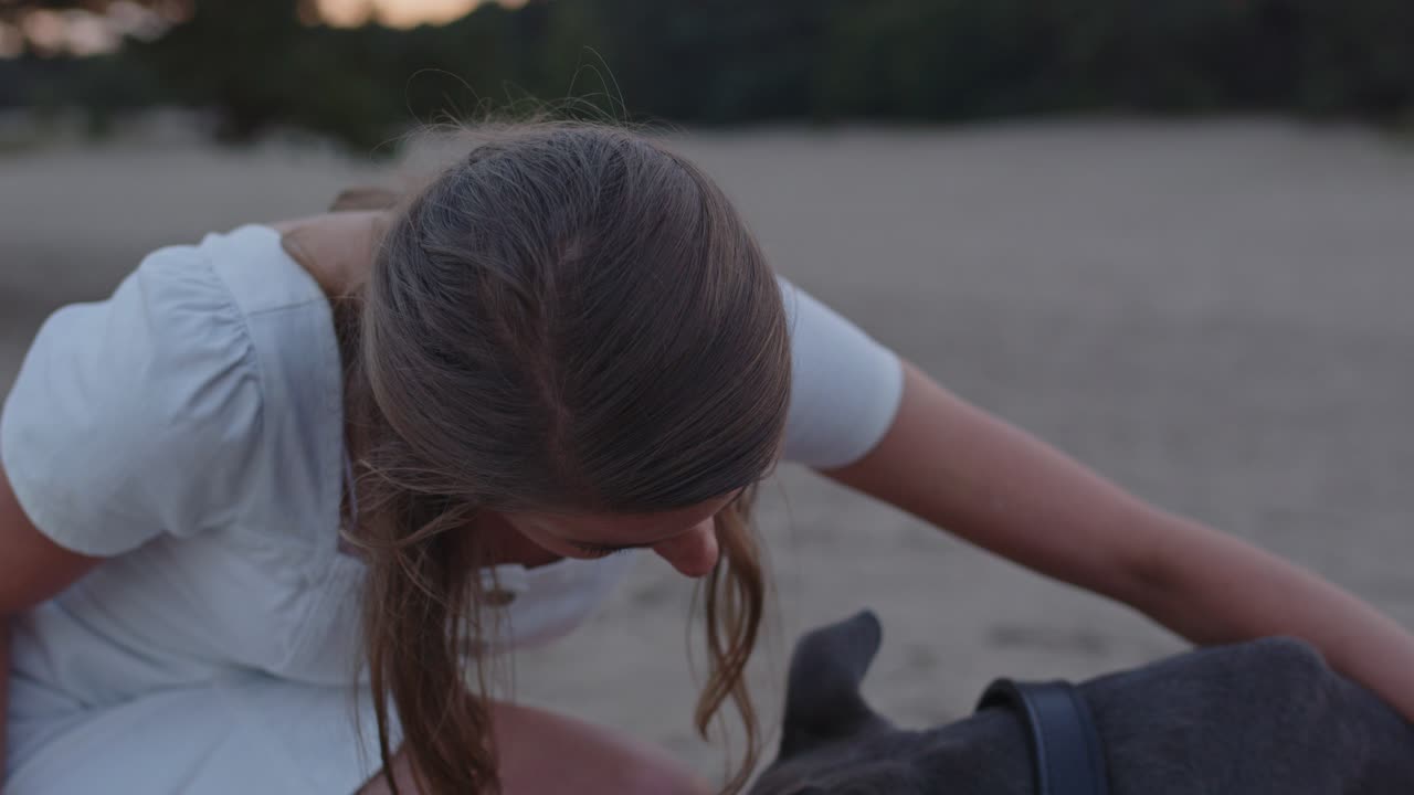 Primo piano di una giovane donna che accarezza il suo cane American Staffordshire Terrier tra le dune di sabbia.