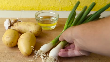 male hand putting green onion on wooden cutting board