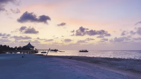 Vista-De-La-Puesta-De-Sol-En-Maldivas:-Vista-Al-Mar-Y-Quietud-Serena-Del-Horizonte-Al-Atardecer-De-La-Isla,-Con-Un-Barco-Dhoni-Tradicional-A-La-Deriva-A-Lo-Largo-Del-Horizonte,-Experiencia-De-Escapada-Tropical-Perfecta