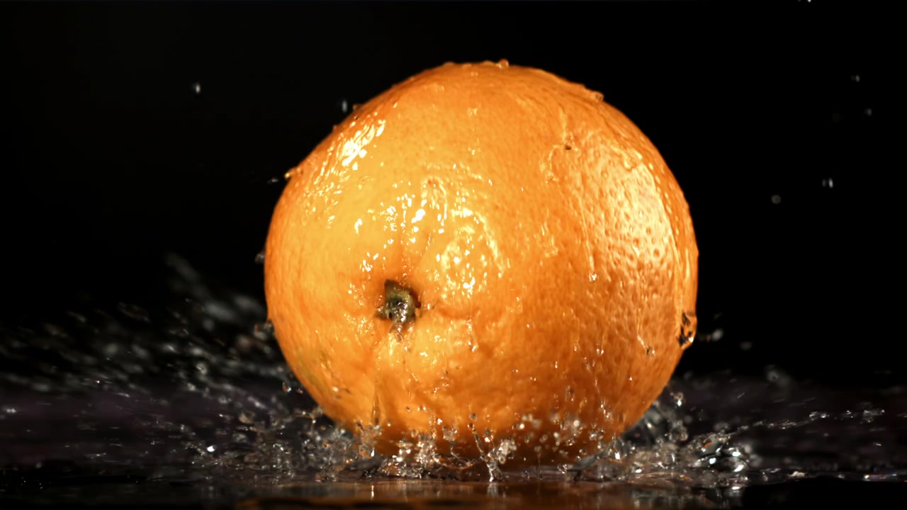 Frisk appelsin plasker ned i vand i slowmotion.