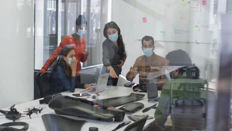 diverse group of work colleagues wearing face masks discussing in meeting room